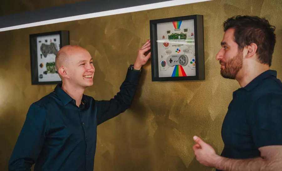 Twee collega's lachen bij de ingelijste game-controllers